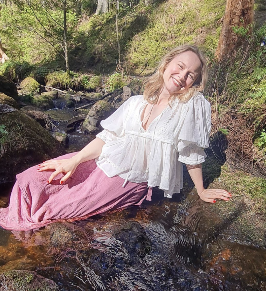 Anna Ma smiling while sitting in a forest stream